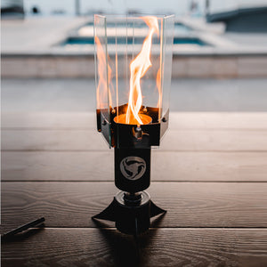 Halo Table Torch - metal and glass table torch lamp with flame spinning in low light of sunset with a luxury pool setting in the background