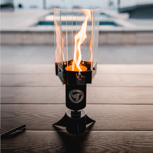 Halo Table Torch - metal and glass table torch lamp with flame spinning in low light of sunset with a luxury pool setting in the background