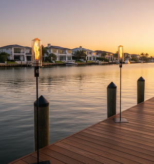 Two outdoor lamps on a dock with a sunset over a waterfront community.