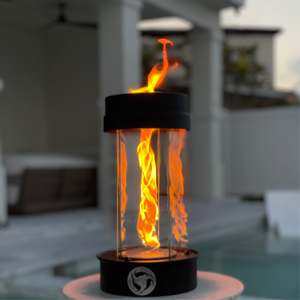 Outdoor oil fire feature with a clear glass wind guard and metal exhaust cap, for use in patio and outdoor living spaces.
