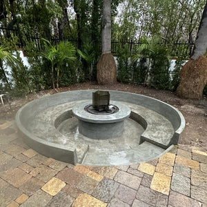 Concrete fire pit with stone patio and trees in the background