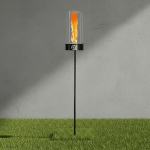 Garden torch with flame on a grassy area against a gray wall