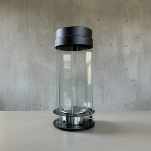 Cylindrical glass container with black metal lid on a concrete surface