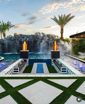 Luxury pool with waterfalls, fire pits, and lounge chairs under a sunset sky.