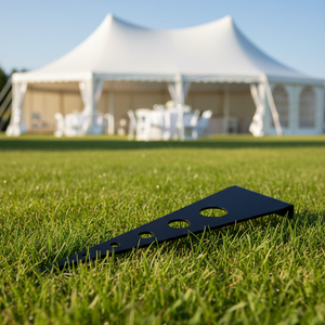 Black cornhole board on grass with a white tent in the background