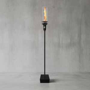 Outdoor gas tiki torch featuring a tall vertical flame, clear glass wind guard, and black metal base for modern patio, garden, and landscape lighting using propane or natural gas.