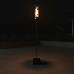 Outdoor gas tiki torch featuring a tall vertical flame, clear glass wind guard, and black metal base for modern patio, garden, and landscape lighting using propane or natural gas.