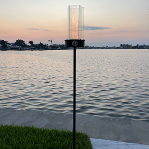 Flickering flame lantern on a stand by a body of water during sunset.