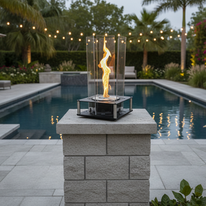 Fire pit on a stone pedestal by a pool with string lights in the background
