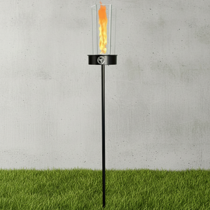 Black outdoor torch with flame on a grassy area against a concrete wall