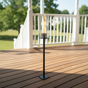 Tiki torch on a wooden deck with a white railing and greenery in the background