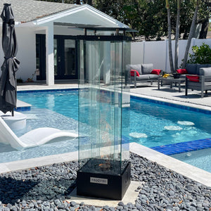 A tall, cylindrical outdoor fire torch with a spinning flame, placed on a pedestal, running on natural gas or propane, set in an outdoor environment.