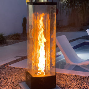 A tall, cylindrical outdoor fire torch with a spinning flame, placed on a stone surface near a pool, showcasing its use in an outdoor setting.