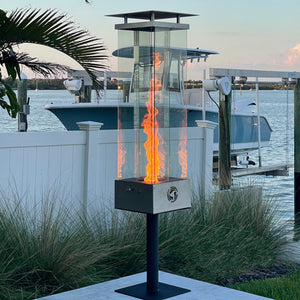 Outdoor fireplace with flames on a patio by a waterfront