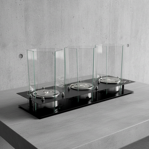 Three metallic objects on a black platform with glass enclosures against a concrete wall.