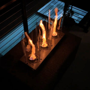 A smokeless triple tornado fireplace set on a hearth, with flames spiraling in opposite directions, illuminated in a dim environment.