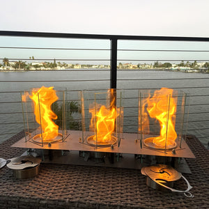 Three fire pits with flames on a patio with a cityscape background