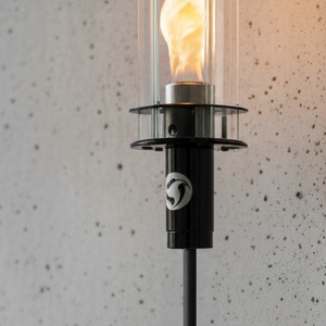Black outdoor torch with a lit flame against a speckled wall background