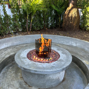 Fire pit with flames in a circular concrete basin surrounded by greenery