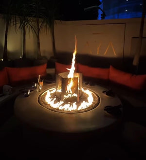 Fire pit with flames at night in an outdoor setting with red cushions and palm trees.