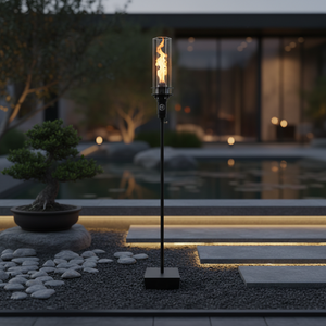 Outdoor gas tiki torch featuring a tall vertical flame, clear glass wind guard, and black metal base for modern patio, garden, and landscape lighting using propane or natural gas.