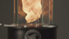 Outdoor oil tabletop fire feature with a vertical flame enclosed in a clear glass wind guard, designed for modern patio tables, outdoor dining areas, and ambient lighting.