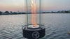 Outdoor oil tabletop fire feature with a vertical flame enclosed in a clear glass wind guard, designed for modern patio tables, outdoor dining areas, and ambient lighting.