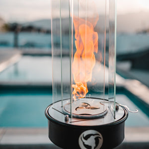 Fire pit with flames inside a transparent container by a poolside.