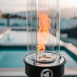 Fire pit with flames inside a glass enclosure by a pool